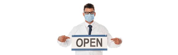 Ausschnitt eines Arztes in medizinischer Maske, der mit den Fingern auf ein Schild mit offenem Schriftzug zeigt, isoliert auf weiß - Foto, Bild
