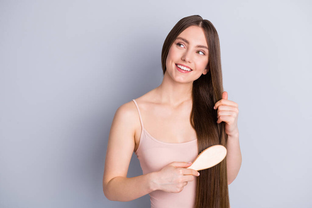 Photo of attractive cheerful model lady long hairdo hold favorite wooden comb carefully brushing strong curls wear beige singlet isolated grey color background - Valokuva, kuva