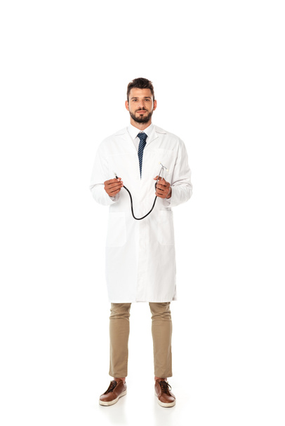Joven médico barbudo de bata blanca sosteniendo estetoscopio aislado en blanco
 - Foto, imagen