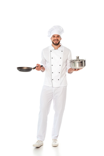 Guapo chef sonriente sosteniendo sartén y sartén sobre fondo blanco
 - Foto, Imagen