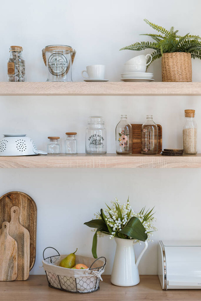 Вертикальное фото кухни с кухонными принадлежностями на деревянных полках, раскройными досками, комнатными растениями, цветами и современной мебелью в минималистском стиле интерьера
 - Фото, изображение