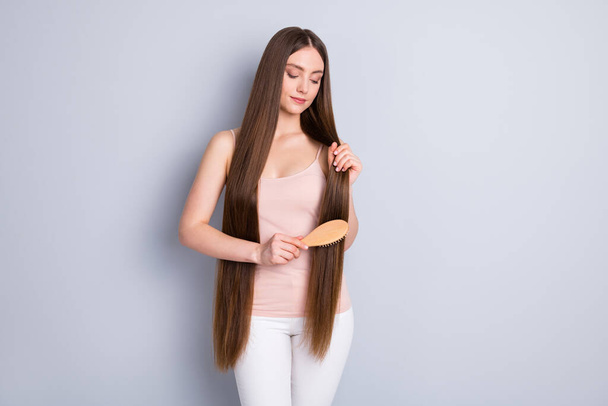 Photo of perfect appearance model lady long hairdo hold favorite wooden comb brushing strong curls wear beige singlet trousers isolated grey color background - Foto, immagini