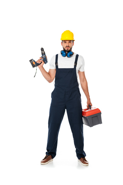 Handsome workman in uniform and hardhat holding electric screwdriver and toolbox on white background - Photo, Image