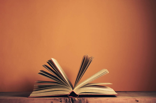 Belo antigo livro antigo aberto em uma mesa de madeira vermelha e fundo de parede laranja atrás. - Foto, Imagem