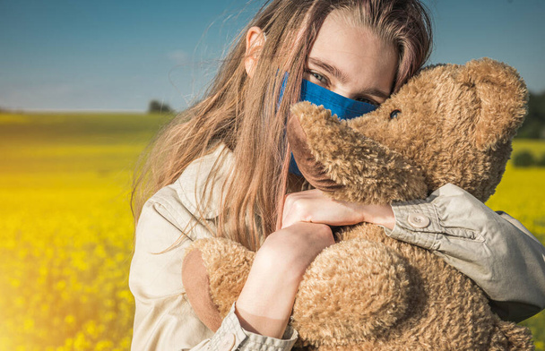 Portrait of Happy Caucasian Teenage Girl in Face Mask Hugging Her Teddy Bear During Pandemic. Virus Outbreak Theme. - Fotoğraf, Görsel