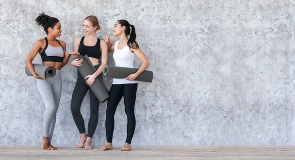 Classe Pilates. Meninas jovens desportivas de pé com tapetes de ioga perto da parede cinza
 - Foto, Imagem