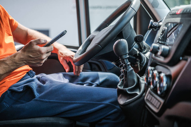 Caucasian Delivery Truck Driver Browsing Internet met behulp van zijn smartphone. Interieur van bestelwagen. - Foto, afbeelding