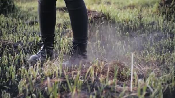Human legs in stylish leather shoes spin in a circle on ashen burnt grass in slow motion in sunny weather. Person is spinning on the burned earth in a field during the day, smoke blowing after a fire. - Footage, Video