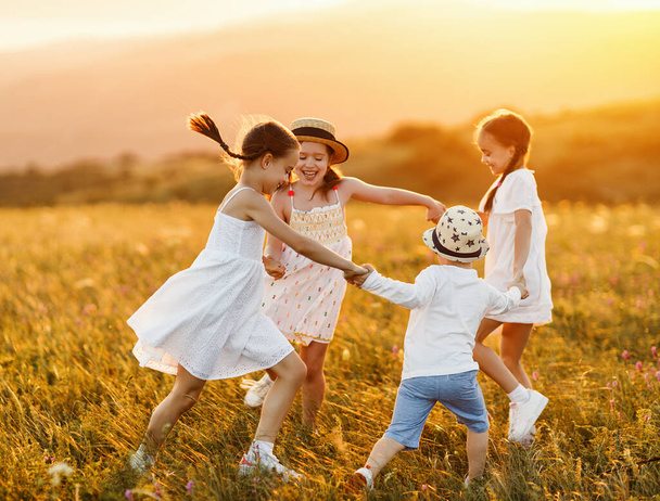 Adorables niñas con hermano menor divirtiéndose y bailando juntos mientras pasan la noche de verano en el prado verde en countrysid
 - Foto, imagen