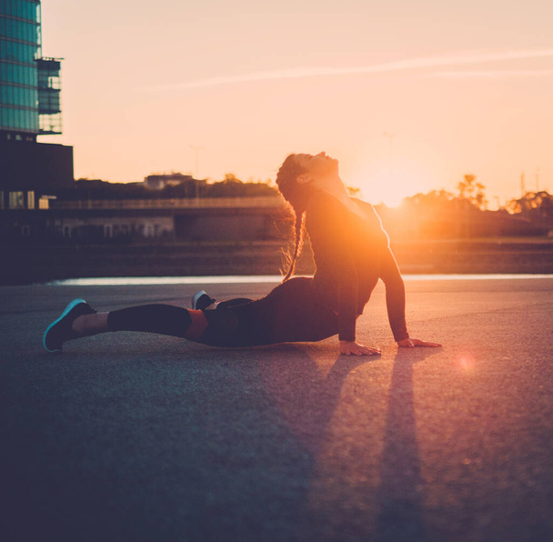 Joven Fitness Mujer Hacer que el cuerpo bajo estiramiento al aire libre en la puesta del sol
. - Foto, imagen