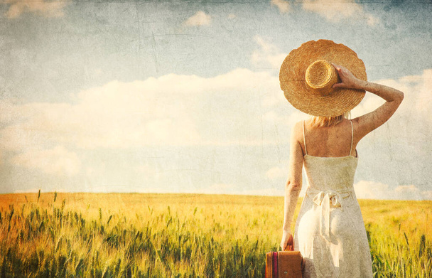 Gün batımında buğday tarlasında bavullu, şapkalı bir kadın.  - Fotoğraf, Görsel