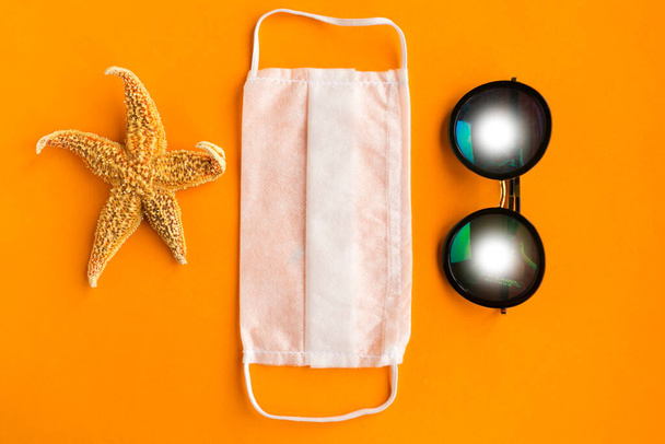 Seestern, medizinische Maske und Sonnenbrille auf orangefarbenem Hintergrund. Coronavirus-Reisekonzept - Foto, Bild