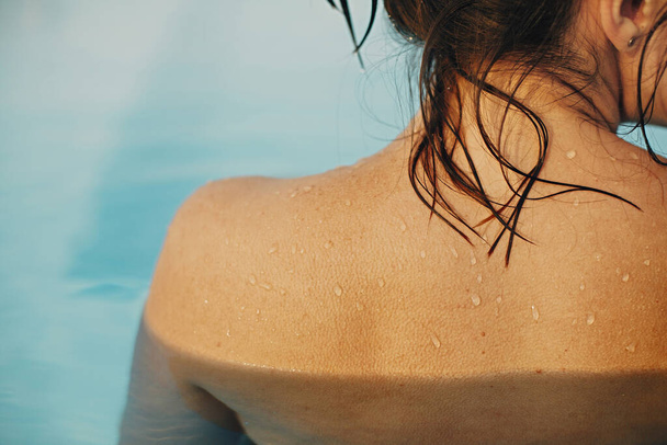 Beautiful woman shoulder with water drops close up, relaxing in pool. Back view of brunette girl with wet skin with goosebumps. Summer vacation. Enjoying summer holiday, swimming in pool - Photo, Image
