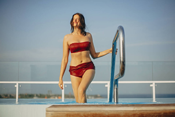 健康な体を持つ幸せな若い女性はプールから出て笑顔。快適な形状の楽しい女の子はリラックスし、豪華な熱帯リゾートの屋上のプールで楽しんでいます。夏休み - 写真・画像