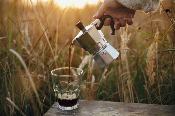 Traveler kaatamalla tuoretta kuumaa kahvia geyser kahvinkeitin osaksi lasi kuppi aurinkoisessa lämpimässä valossa maaseudulla yrttejä. Ilmakehän rauhallinen hetki. Vaihtoehtoinen kahvi panimo matkoilla - Valokuva, kuva