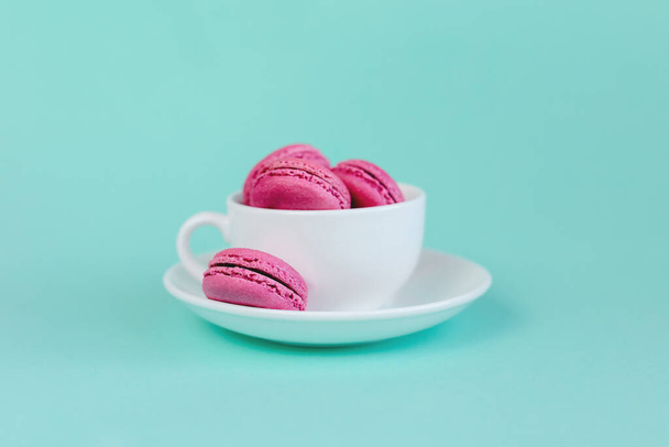 Смачні рожеві французькі рожеві макаруни в білій чашці на бірюзовому фоні. Місце для тексту
. - Фото, зображення