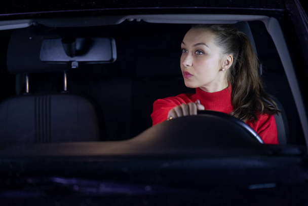 smiling brunette long hair girl in car driving at night looks in rearview mirror - Zdjęcie, obraz