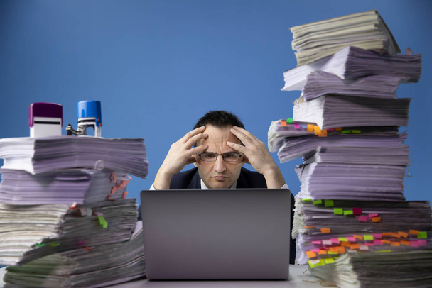 Zmęczony zaniepokojony biznesmen siedzi przy biurku z ogromną stertą dokumentów - Zdjęcie, obraz