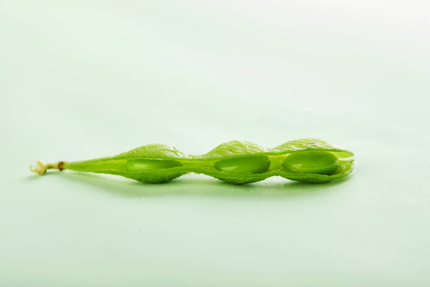 An opened pod of Edamame or soybeans is isolated on a turquoise background. - Φωτογραφία, εικόνα