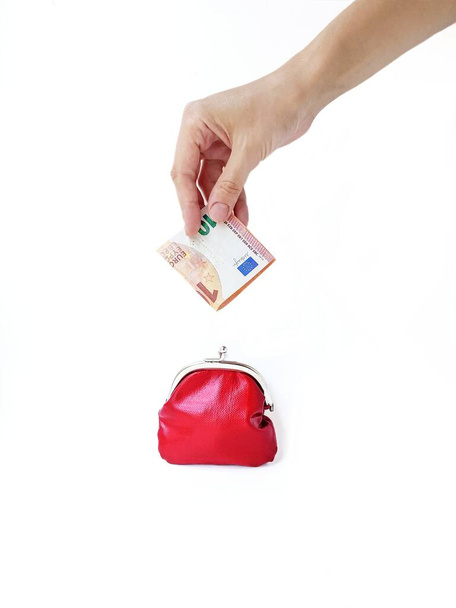 Жіноча рука кладе гроші в червоний гаманець з металевим замком на білому тлі. Економія грошей
. - Фото, зображення