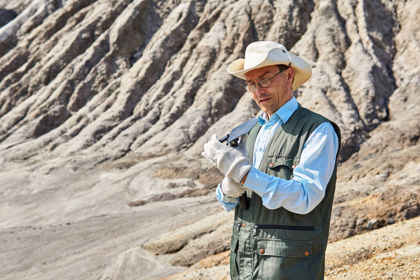 male researcher prepares for work a folding shovel against a desert landscape - Foto, imagen
