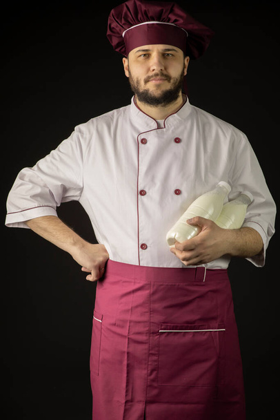 Handsome bearded chef man in uniform holds two bottles with milk - Photo, Image