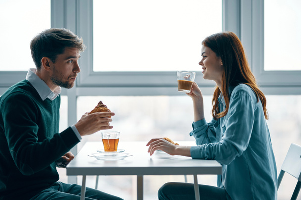 Ein Mann mit einem Croissant in der Hand hält eine Tasse Tee und eine Frau mit Kaffee - Foto, Bild