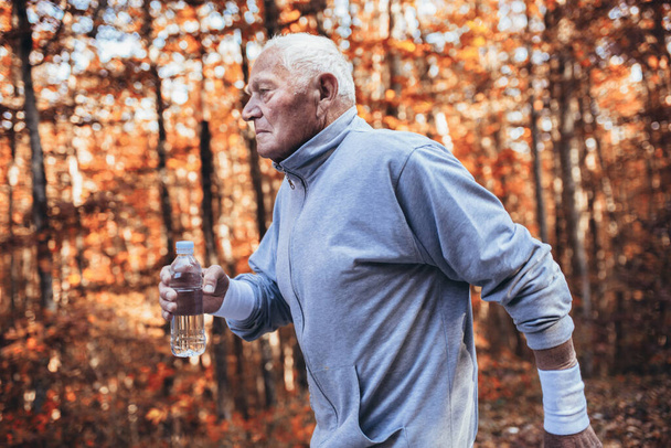 Doğanın kıdemli koşucusu. Yaşlı sporcu adam sabah antrenmanı sırasında ormanda koşuyor. Her yaş kavramında sağlıklı ve aktif bir yaşam tarzı - Fotoğraf, Görsel