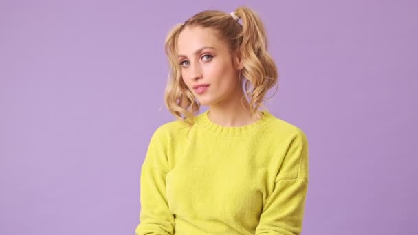 A cute blonde smiling, flirting at the camera, biting her lip and raising eyebrows in an isolated studio on a purple background - Séquence, vidéo