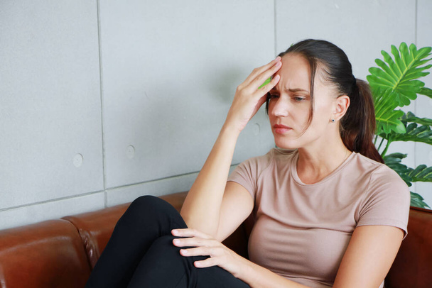 Kafkasyalı genç kadın kahverengi kanepede depresyon ve baş ağrısı çekiyor ve toplumda sorunlar yaşadığı için stresli..  - Fotoğraf, Görsel