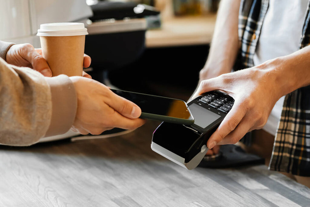 Bir adam bir kahve dükkanında bir fincan kahve için akıllı telefonla ödeme yapar. Satın alma kavramı - Fotoğraf, Görsel