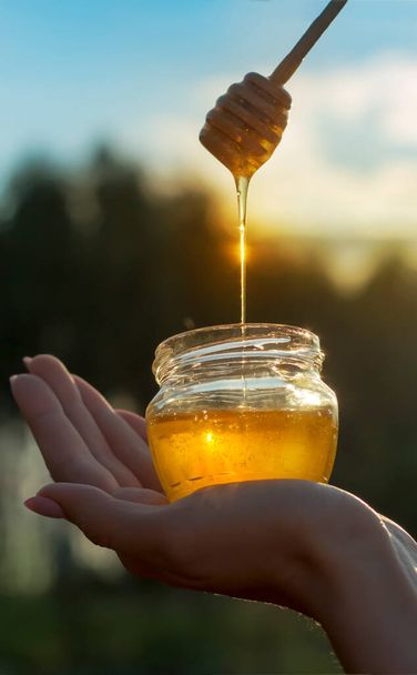 the girl holds a jar of honey in the palm of her hand, honey is poured into the jar from a spoon. - Photo, Image