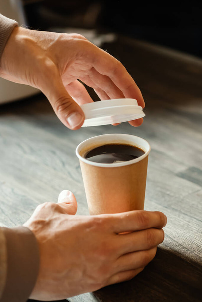 A man bought coffee in a paper cup and closes it with a plastic lid. Takeaway food and drink concept. - Photo, Image