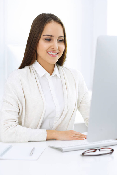 Business woman sitting and working with computer in white office. Student girl studying or secretary making report. Success concept - Zdjęcie, obraz