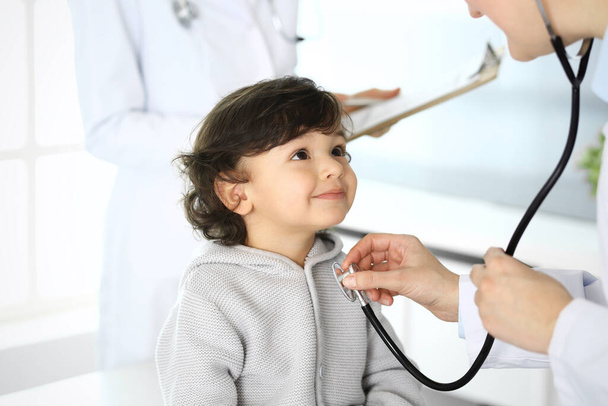 Врач осматривает ребенка стетоскопом. Милый арабский мальчик на приеме у врача. Медицина и здравоохранение - Фото, изображение