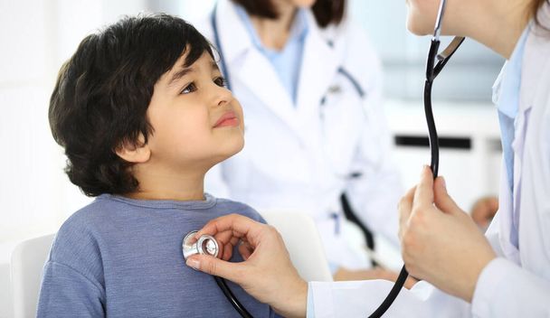 Doctor examining a child patient by stethoscope. Cute arab boy at physician appointment. Medicine and healthcare concept - Photo, image