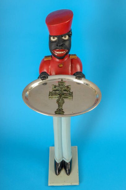 Estátua de um servo negro com uma cruz religiosa em uma bandeja
 - Foto, Imagem