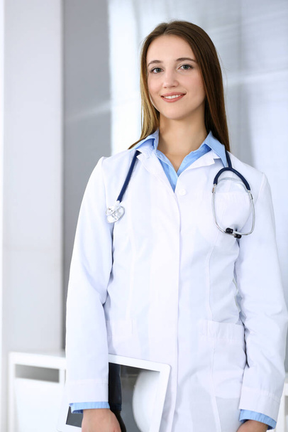 Doctor woman happy and cheerful while standing in hospital office at highlight background. Medicine and healthcare concept - Фото, изображение