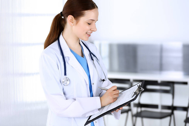 Doctor woman or intern student at work. Physician filling up medication history record while standing in emergency hospital office. Medicine and health care concept - Photo, image