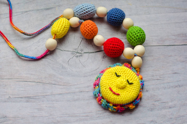 Collier en perles tricotées et jouets pour le bébé assis dans une fronde. Perles tricotées. Collier fronde. - Photo, image