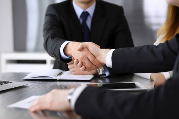 Businessman shaking hands with his colleague or partner above the glass desk in modern office, close-up. Unknown business people at meeting. Teamwork, partnership and handshake concept - Foto, immagini