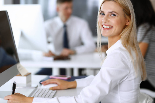 Modern ofisteki işyerinde bilgisayar kullanan bir iş kadını. Sekreter ya da kadın avukat gülümsüyor ve mutlu görünüyor. Zevk ve başarı için çalışmak - Fotoğraf, Görsel