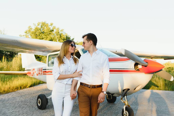 Full-length image of beautiful young stylish couple near private plane. Walking on runway in airport in front of airplane. - Photo, Image