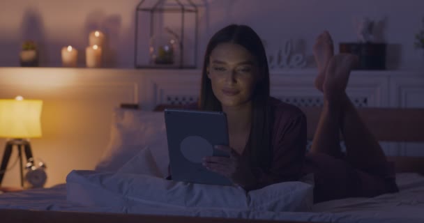 Woman networking on digital tablet, lying in pajamas in bed - Filmati, video