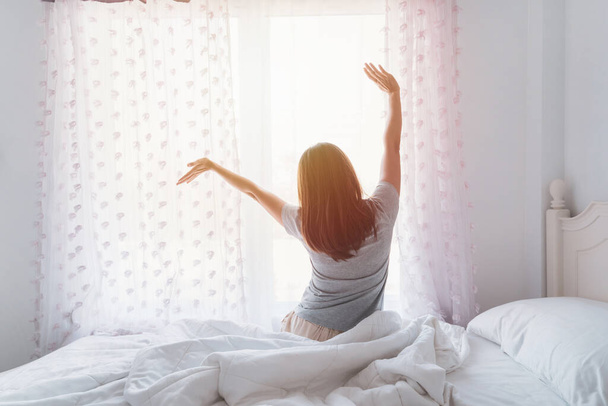 Young asian woman sitting on the bed and stretch oneself in the morning - Foto, afbeelding