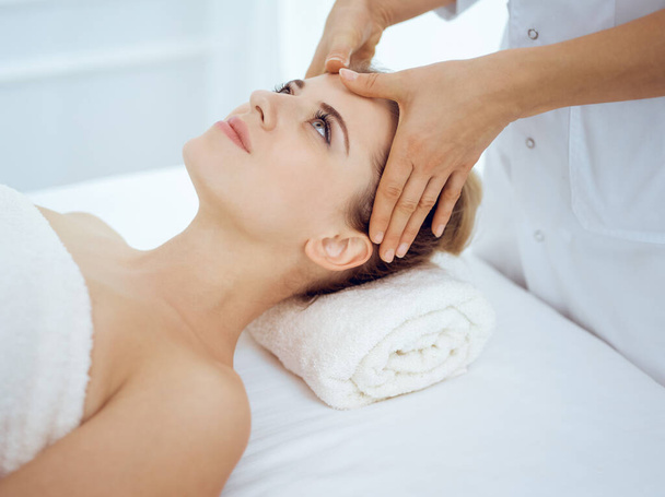 Young and blonde woman enjoying facial massage in spa salon. Beauty concept - Photo, image