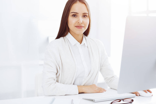 Business woman sitting and working with computer in white office. Student girl studying or secretary making report. Success concept - Foto, afbeelding