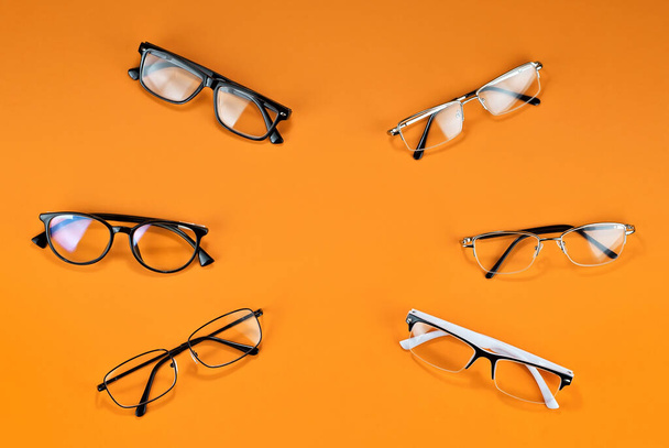 Different types of glasses on an orange background close up. Glasses with rectangular and round frames. Layout for design. Space for text and free space near the object. - Photo, image