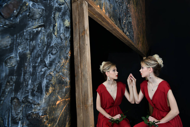 hermosa chica en vestido de noche borgoña por el espejo con su reflejo sobre un fondo negro
 - Foto, imagen