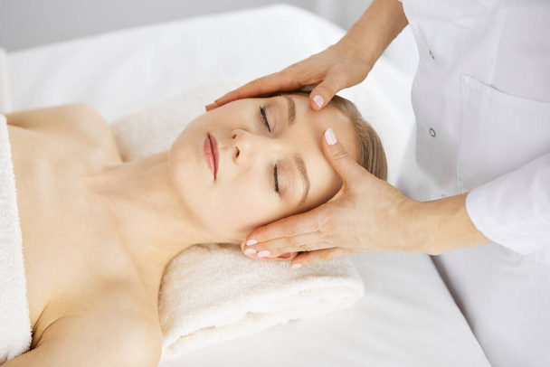 Beautiful caucasian woman enjoying facial massage with closed eyes in spa salon. Relaxing treatment in medicine and Beauty concept - Fotó, kép